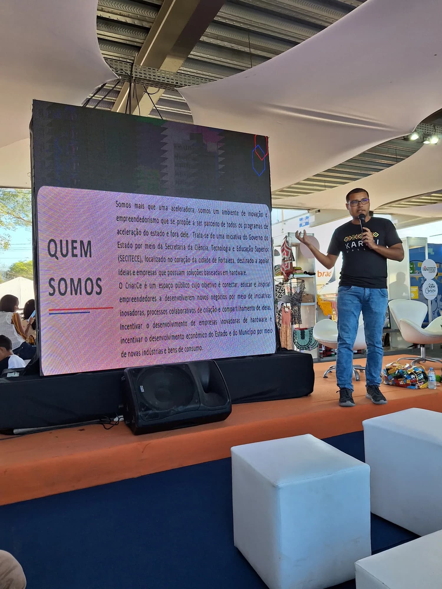 Participante apresenta a comunidade ao lado de um painel durante um encontro